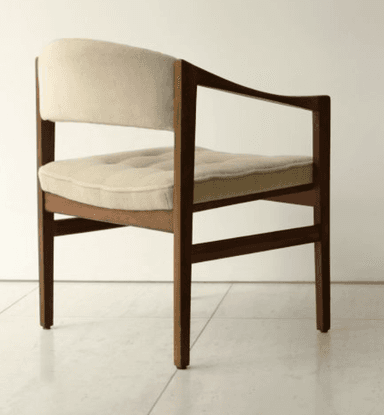 A mid-century modern armchair featuring a dark wood frame and light beige fabric upholstery. The chair has a clean, rectilinear wooden frame with subtly curved armrests. Both the seat and back are padded, with the seat cushion exhibiting button tufting, suggesting a comfortable yet structured design. The wooden legs are straight, and the overall aesthetic is minimalist and functional. — 3D model