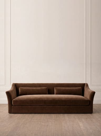 A contemporary two-seater sofa upholstered in a rich brown velvet or plush fabric, featuring gently flared arms and two rectangular bolster-style back cushions. The sofa has a low-profile design with a fully upholstered base that extends to the floor, concealing any legs. The overall aesthetic is one of comfort and modern sophistication. — 3D model