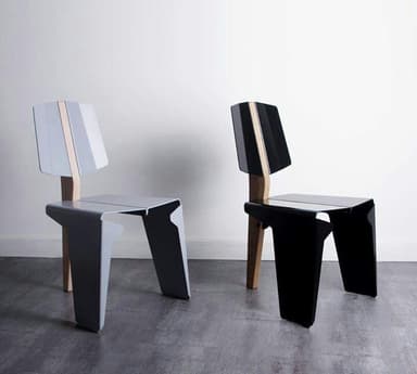 A contemporary armless side chair featuring a distinctive two-tone design, composed primarily of angular black panels for the seat and front legs, complemented by a natural wood element that forms the rear support and spine of the backrest. The chair exhibits a minimalist and geometric aesthetic. — 3D model