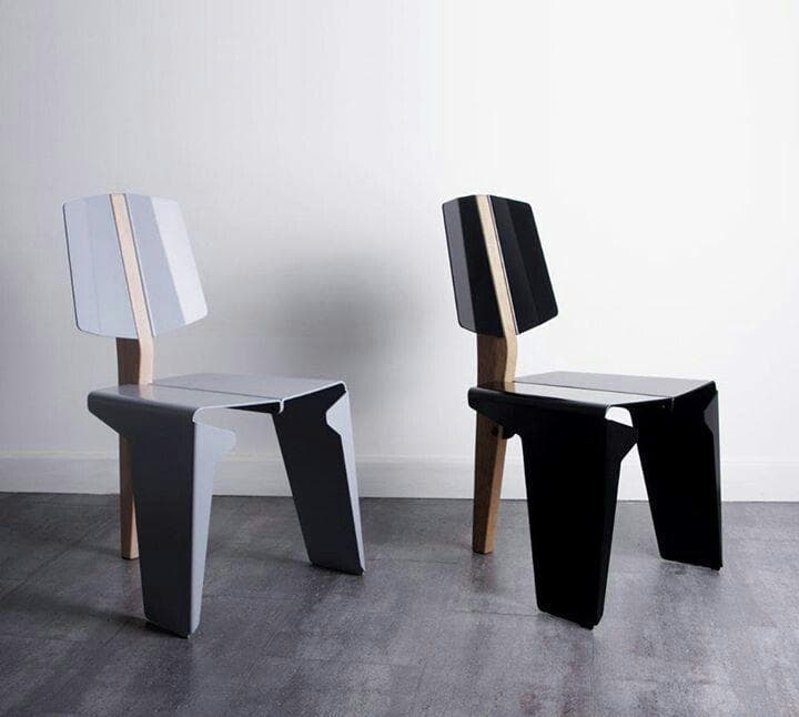 A contemporary armless side chair featuring a distinctive two-tone design, composed primarily of angular black panels for the seat and front legs, complemented by a natural wood element that forms the rear support and spine of the backrest. The chair exhibits a minimalist and geometric aesthetic. — 3D model