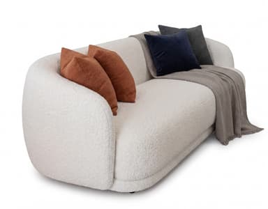 A contemporary, curved sofa upholstered in a textured cream-colored boucle fabric, featuring a smooth, organic silhouette without visible legs. The sofa includes several accent pillows in varying textures and colors, specifically two rust-colored boucle pillows, one dark blue velvet pillow, and one charcoal gray fabric pillow, along with a light grey herringbone throw blanket draped over its seat and backrest. — 3D model