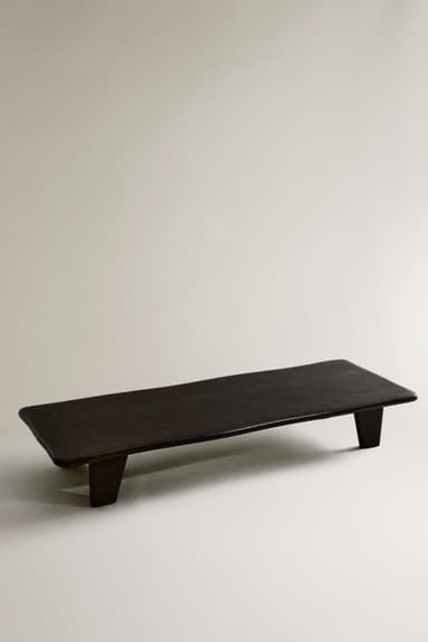 A minimalist, rectangular display riser or monitor stand, crafted from dark brown wood with a smooth, matte finish. It features a flat top surface with gently rounded edges and is supported by two integrated, block-like feet positioned towards the ends of the base. — 3D model