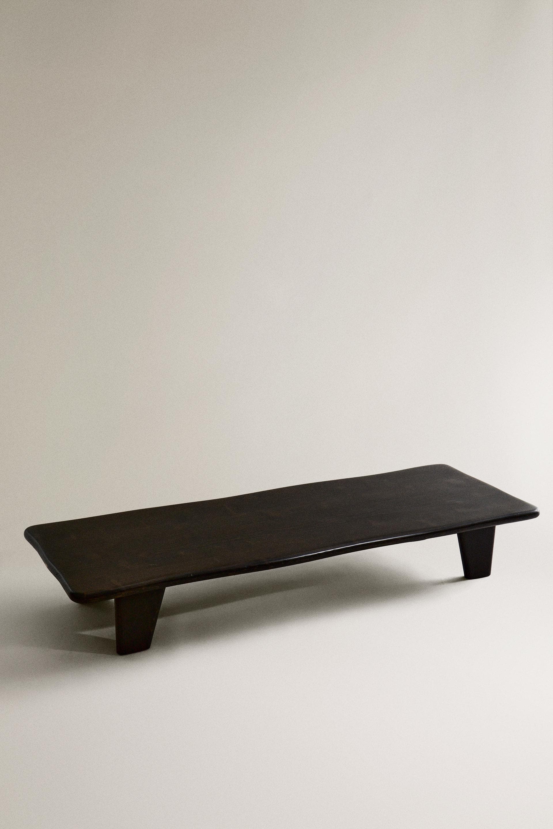 A minimalist, rectangular display riser or monitor stand, crafted from dark brown wood with a smooth, matte finish. It features a flat top surface with gently rounded edges and is supported by two integrated, block-like feet positioned towards the ends of the base. — 3D model
