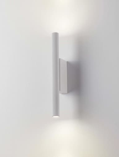 A contemporary white wall sconce featuring a vertical, cylindrical body with a distinctive ribbed texture. The fixture is mounted directly to the wall and emits light from both its upper and lower ends, providing an up-and-down illumination effect. — 3D model