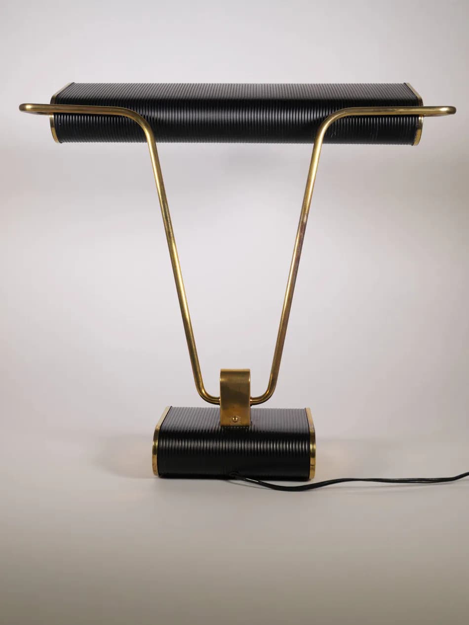 A stylish mid-century industrial desk lamp featuring a horizontal, rectangular, ribbed black shade and a matching ribbed black rectangular base. It is supported by two V-shaped polished brass arms that connect the shade to the base, with a central brass accent bracket. — 3D model