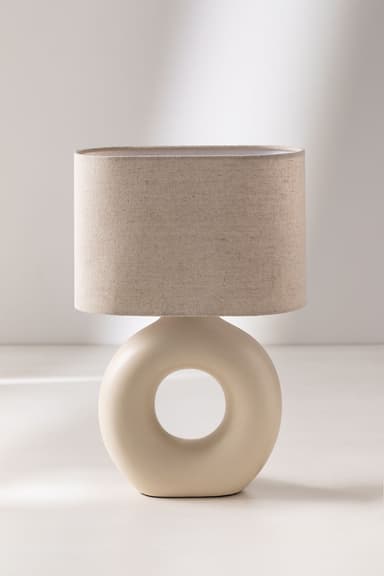 A modern table lamp featuring a cream-colored ceramic torus-shaped base with a central cut-out, topped with a cylindrical light beige fabric shade. — 3D model