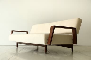 A minimalist two-seater loveseat featuring a cream-colored upholstered seat and backrest, supported by a dark, possibly walnut, wooden frame with open, U-shaped armrests and slender tapered legs. — 3D model