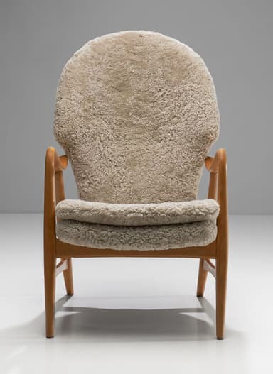 A high-backed armchair with a wooden frame and plush sheepskin upholstery. The frame consists of curved wooden arms and legs. The seat and back are fully upholstered in a textured, cream-colored sheepskin material, giving it a soft and inviting appearance. The design suggests a focus on comfort and organic forms. — 3D model