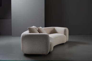 A contemporary, low-profile sofa upholstered in a cream-colored boucle fabric, featuring soft, rounded edges and a subtly curvilinear form, accompanied by two matching throw pillows. — 3D model