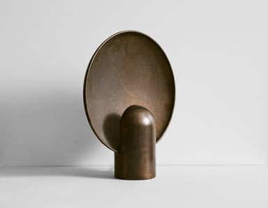 A golden-hued, abstract decorative object made of brass, featuring a large, textured, concave circular disc mounted on a smaller, smooth, rounded pedestal base. The disc has an irregular, almost hammered texture, while the base is smooth and reflective. The object has a substantial, solid appearance. — 3D model