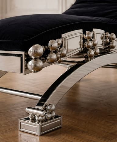 A luxurious and modern chaise lounge featuring a highly polished chrome or silver-toned metal frame with a black velvet upholstered body. The frame is intricately designed with decorative spherical accents and a sculptural, curvilinear base. The seating surface is tufted, and there is an integrated cylindrical headrest. The overall aesthetic is one of modern glamor and opulence. — 3D model