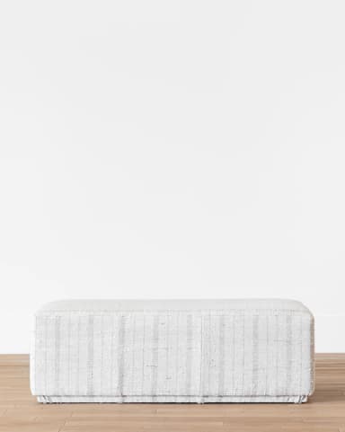 A rectangular upholstered ottoman featuring a subtle light grey and white striped fabric pattern. The object has a simple, block-like form with a low profile and appears to be softly padded. — 3D model