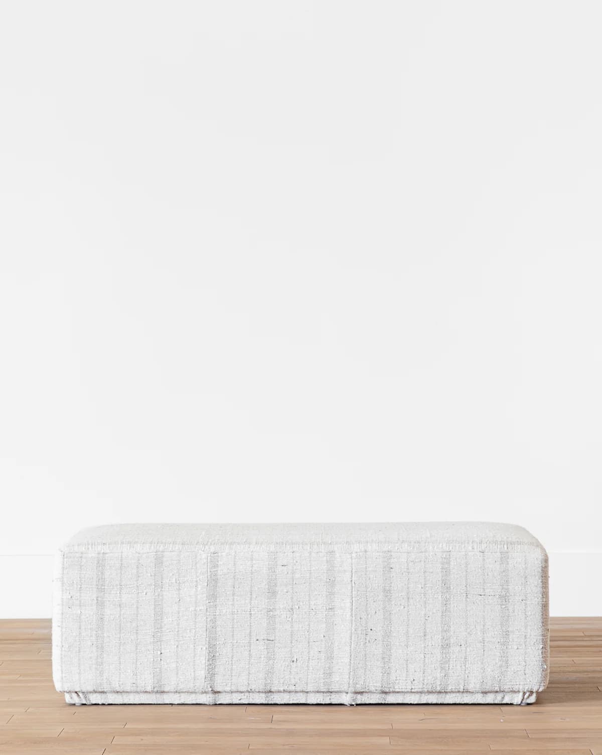 A rectangular upholstered ottoman featuring a subtle light grey and white striped fabric pattern. The object has a simple, block-like form with a low profile and appears to be softly padded. — 3D model