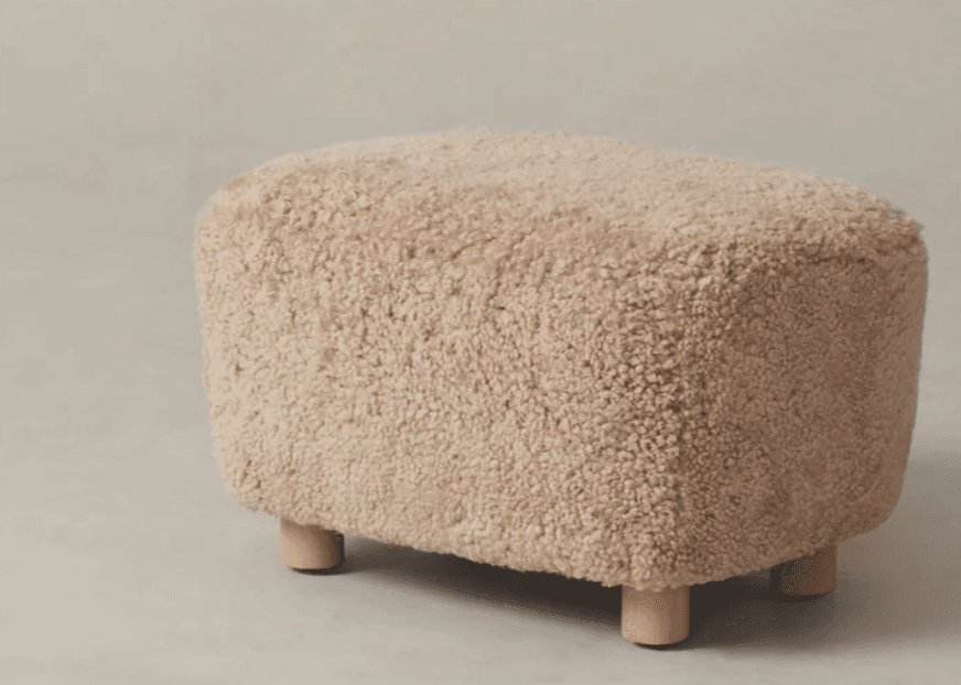A rectangular ottoman with rounded edges, covered in a textured, fluffy, off-white material resembling sheepskin. It is supported by four short, cylindrical wooden legs. — 3D model