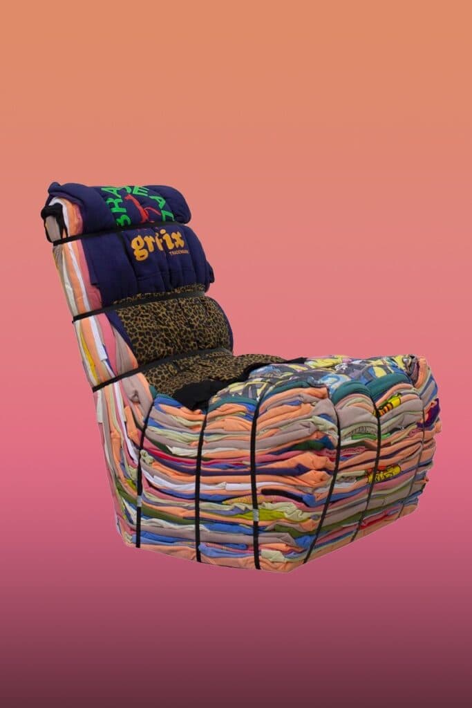 A unique lounge chair constructed entirely from tightly bundled and strapped clothing and textile scraps, forming a distinct backrest and seat. The various fabrics create a multicolored, textured surface, held together by visible black strapping bands. — 3D model