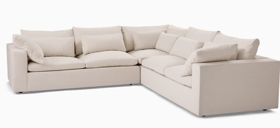 A large, L-shaped sectional sofa featuring deep, plush seating and back cushions. The sofa is upholstered in a light, neutral fabric, likely linen or a linen blend, and sits low to the ground on discreet, small feet. It appears to be modular, allowing for flexible configurations, with wide, flat arms and generous back cushions providing ample support for a relaxed aesthetic. — 3D model