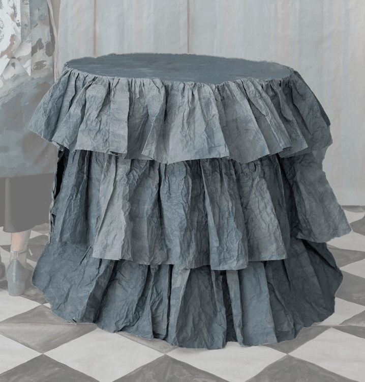 A cylindrical accent table entirely covered in multiple tiers of ruffled, crumpled blue-grey fabric, presenting a soft and textural appearance. — 3D model