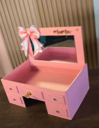 A miniature pink vanity unit designed for tabletop use, featuring a mirrored back panel with the word 'mama' inscribed, and decorative elements such as a bow and a crystal drawer pull. It has multiple small drawers for storage. — 3D model