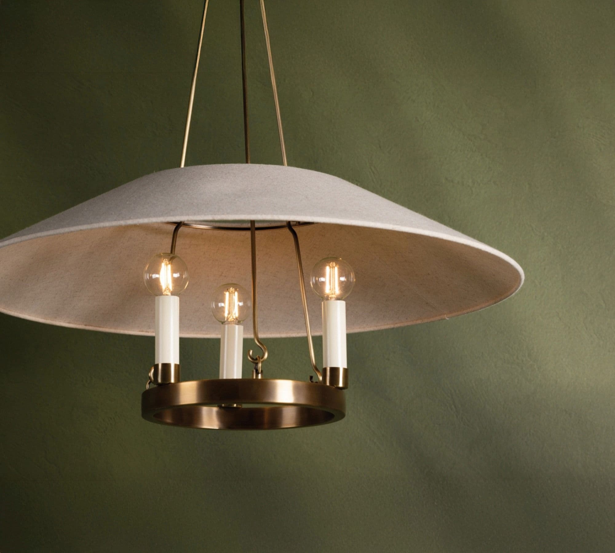 A modern chandelier featuring a wide, shallow, inverted dome-shaped lampshade made of light gray fabric. Beneath the fabric shade, a polished brass ring holds three vertically oriented light sockets, each fitted with a candle-style LED bulb. The fixture is suspended by thin brass rods, contributing to its minimalist and elegant aesthetic. The light emitted by the bulbs is diffused by the fabric shade, creating a soft, ambient glow. — 3D model