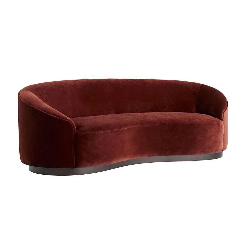 A curved sofa with a plush velvet upholstery in a deep reddish-brown hue. The sofa features a rounded silhouette with integrated armrests and a low-profile base. The base appears to be made of a darker material, possibly wood or metal, with a smooth finish and a slightly curved profile that mirrors the overall shape of the sofa. — 3D model