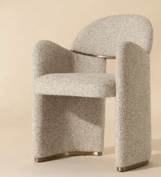 An upholstered accent chair with a distinctive sculptural form, featuring integrated curved backrest and armrests. The chair is covered in a light-colored, textured bouclé fabric. Its solid, block-like base and armrests curve gently, meeting brass-finished accents at the floor level. The overall design suggests a modern or contemporary aesthetic. — 3D model