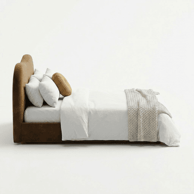 A modern upholstered bed featuring a distinctive wavy headboard and a low-profile frame. The bed is covered in a rich, brown velvet-like fabric, presenting a soft and luxurious appearance. It is dressed with clean white bedding, including two standard pillows and a duvet, accented by a round mustard-colored velvet pillow and a chunky knit beige throw blanket draped across the foot of the bed. The overall design emphasizes organic shapes and contemporary elegance. — 3D model