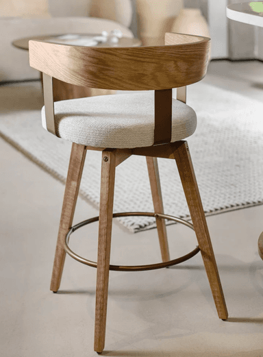 A modern swivel bar stool featuring a light-toned wooden frame, a plush upholstered seat, and a distinctive curved wooden backrest. It stands on four tapered wooden legs, reinforced by a circular metal footrest, and features a visible swivel mechanism. — 3D model