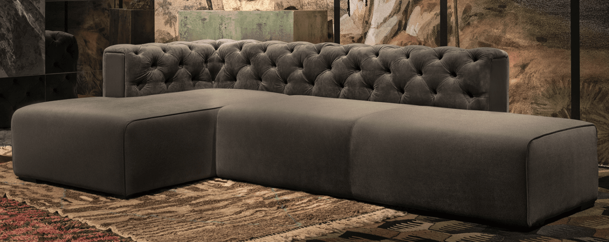 A modular sectional sofa with a tufted backrest on one section and plain upholstered seating modules. The sofa is upholstered in a dark grey fabric and is configured in an L-shape. The backrest features deep button tufting in a diamond pattern. The seating modules have a modern, minimalist design with clean lines and are supported by low-profile dark feet. — 3D model