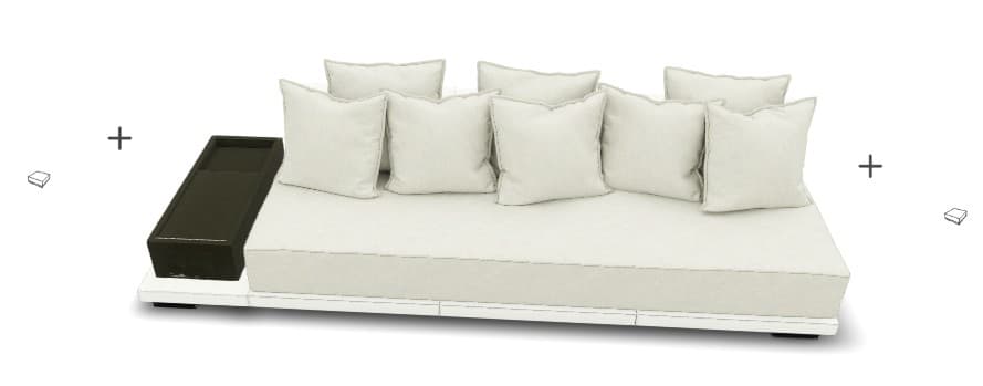 A contemporary, low-profile sofa with a modular design. It features a white base frame and a large, flat seat cushion. Several rectangular, off-white throw pillows are arranged against the back. A dark brown, rectangular side table is attached to the left side of the sofa. The overall aesthetic suggests an outdoor or lounge setting. — 3D model