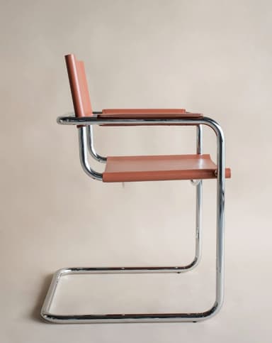 A modern armchair with a tubular chrome frame and leather upholstery. The seat and backrest are made of brown leather straps, and the armrests are also upholstered in leather. The frame is constructed from bent tubular metal, forming legs that extend upwards to support the seat and back. — 3D model
