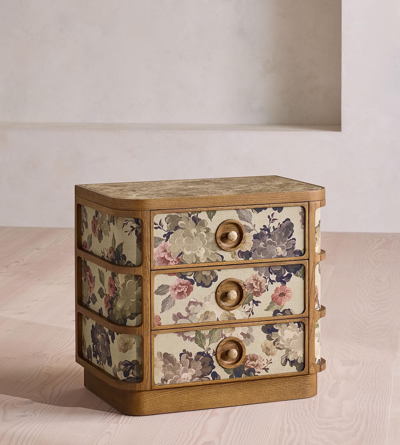 A three-drawer chest of drawers with a wooden frame and a marble or stone-effect top. The drawer fronts and sides are covered in fabric with a floral pattern. Each drawer has a circular wooden knob. The base has a curved, stepped design. — 3D model