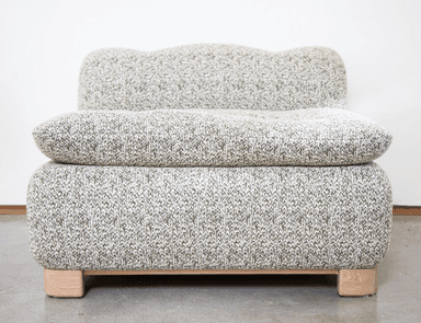 A contemporary armchair with a distinctive rounded silhouette. The piece is upholstered in a textured knit fabric with a marled pattern of light grey and white. It features a low profile, a generously padded seat cushion, and a softly curved backrest. The armchair is supported by a minimalist wooden base with four block-like feet. — 3D model