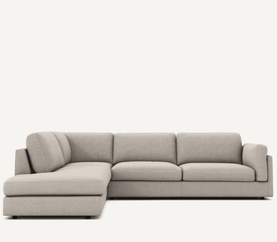 An L-shaped sectional sofa in a light beige or greige fabric, featuring clean lines, low-profile block arms, and a comfortable chaise lounge extension on the left side. The sofa is composed of modular-looking sections with defined seat and back cushions. — 3D model