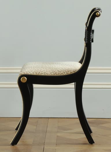 A black wooden side chair featuring a distinctive Regency or Neoclassical design. It has elegantly curved sabre legs and a scrolled backrest, both adorned with gold trim. The backrest also incorporates a rope-twist detail. The seat is upholstered in a light, neutral fabric with a subtle animal print. — 3D model