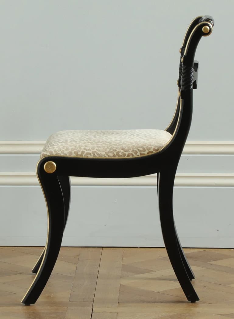 A black wooden side chair featuring a distinctive Regency or Neoclassical design. It has elegantly curved sabre legs and a scrolled backrest, both adorned with gold trim. The backrest also incorporates a rope-twist detail. The seat is upholstered in a light, neutral fabric with a subtle animal print. — 3D model