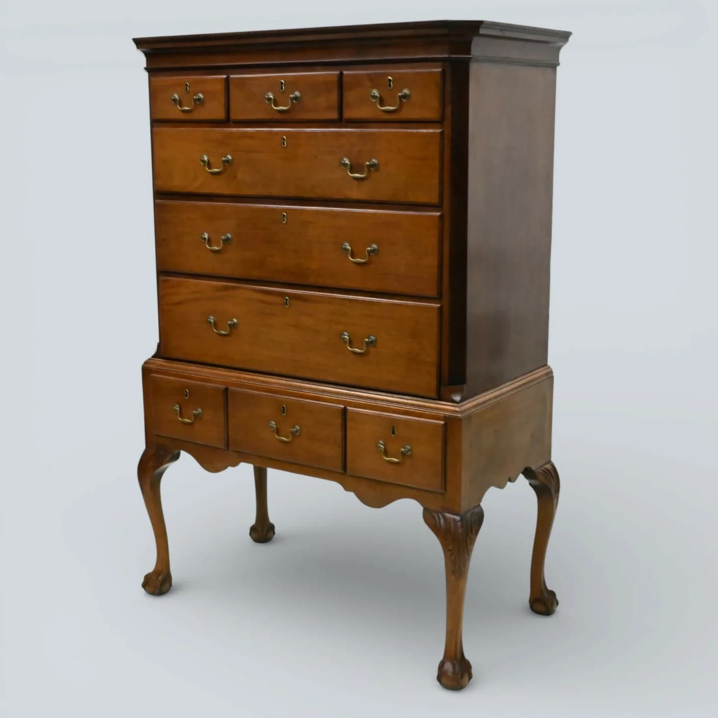 A traditional Queen Anne style highboy chest of drawers, constructed from medium-toned polished wood, featuring two stacked sections of multiple drawers with brass bail pulls, and supported by ornate cabriole legs ending in claw-and-ball feet. — 3D model