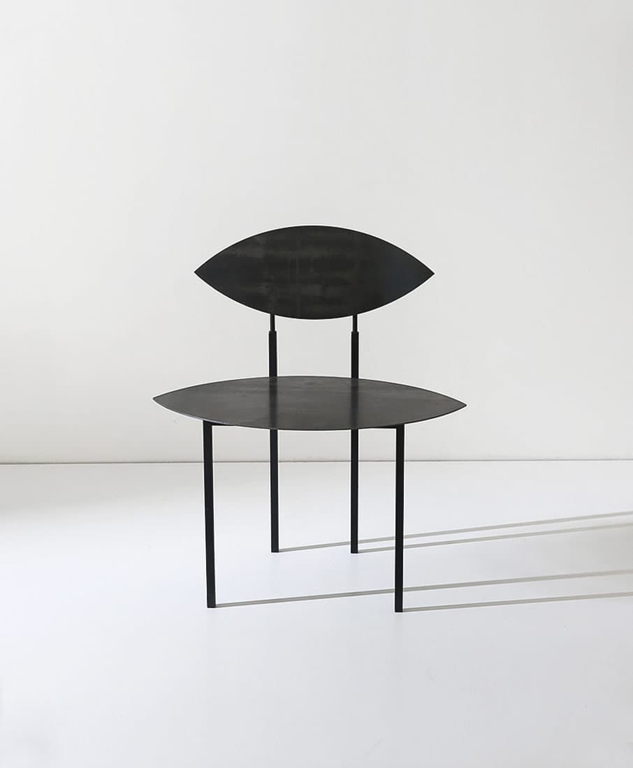 A minimalist black metal chair featuring a sculptural design with lenticular, eye-shaped seat and backrest, supported by thin cylindrical legs. — 3D model