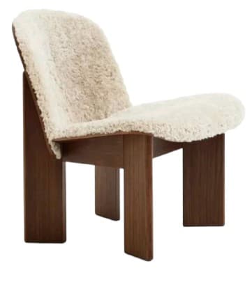 A low-profile armchair with a wooden frame and a textured, sheepskin-like upholstery covering the seat and backrest. The frame has a minimalist design with thick, rectangular legs and a supporting structure for the seat and back. The upholstery is a light, creamy color and appears to be soft and plush. — 3D model