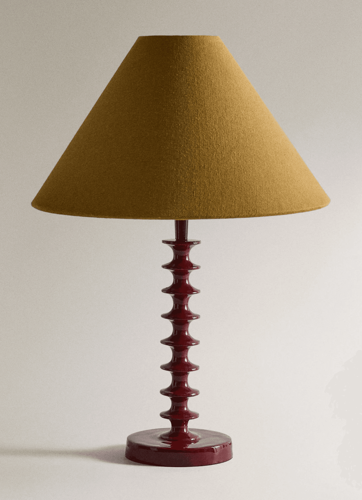 A table lamp featuring a distinctive dark red, glossy lacquered wood base with multiple turned 'spool' or 'bobbin' segments, topped by a conical lampshade made of textured yellow-ochre fabric. — 3D model