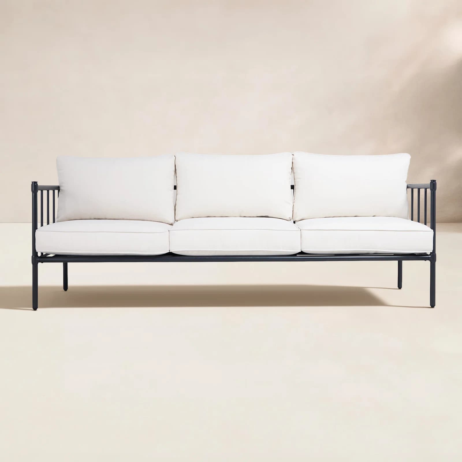 A minimalist three-seater outdoor sofa featuring a sleek black metal frame and three plush, off-white seat cushions and back cushions. The frame is constructed from slender, powder-coated metal tubing with integrated vertical bar armrests and back support. The design is contemporary and functional, ideal for outdoor living spaces. — 3D model