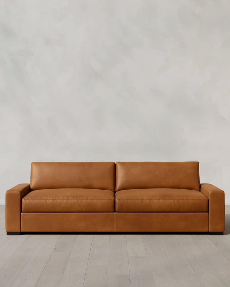 A contemporary sofa upholstered in smooth, tan-colored leather, featuring two wide seat cushions and two back cushions. It has wide, block-style armrests and a low profile supported by discreet, dark block feet. — 3D model