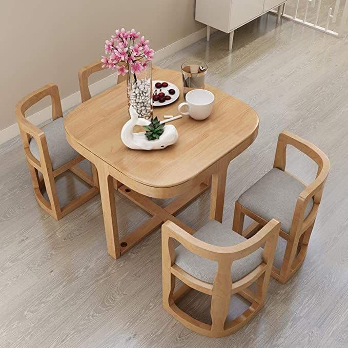 A compact modern dining set featuring a square wooden table with rounded corners and four matching chairs, each with a grey upholstered seat. The table has a distinctive X-shaped base for stability. The chairs feature curved, open-frame backs and integrated armrests, designed for small spaces. — 3D model