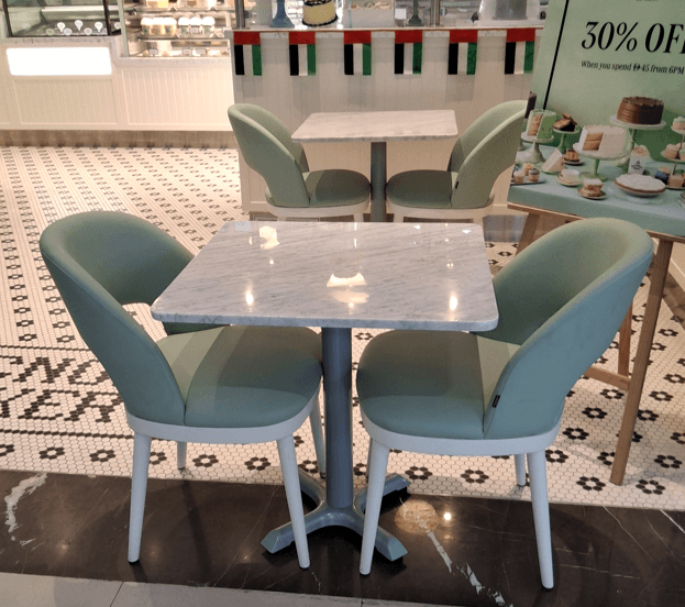 A modern dining set featuring a square table with a white marble top and a grey pedestal base, paired with two upholstered dining chairs. The chairs have light green fabric upholstery, a curved bucket-style seat and back, a small cutout in the lower back, and light-colored, slightly tapered legs. — 3D model