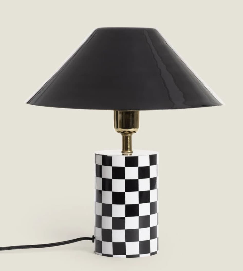 A contemporary table lamp featuring a cylindrical base adorned with a black and white checkerboard pattern, a brass-finished stem, and a glossy black conical shade. — 3D model