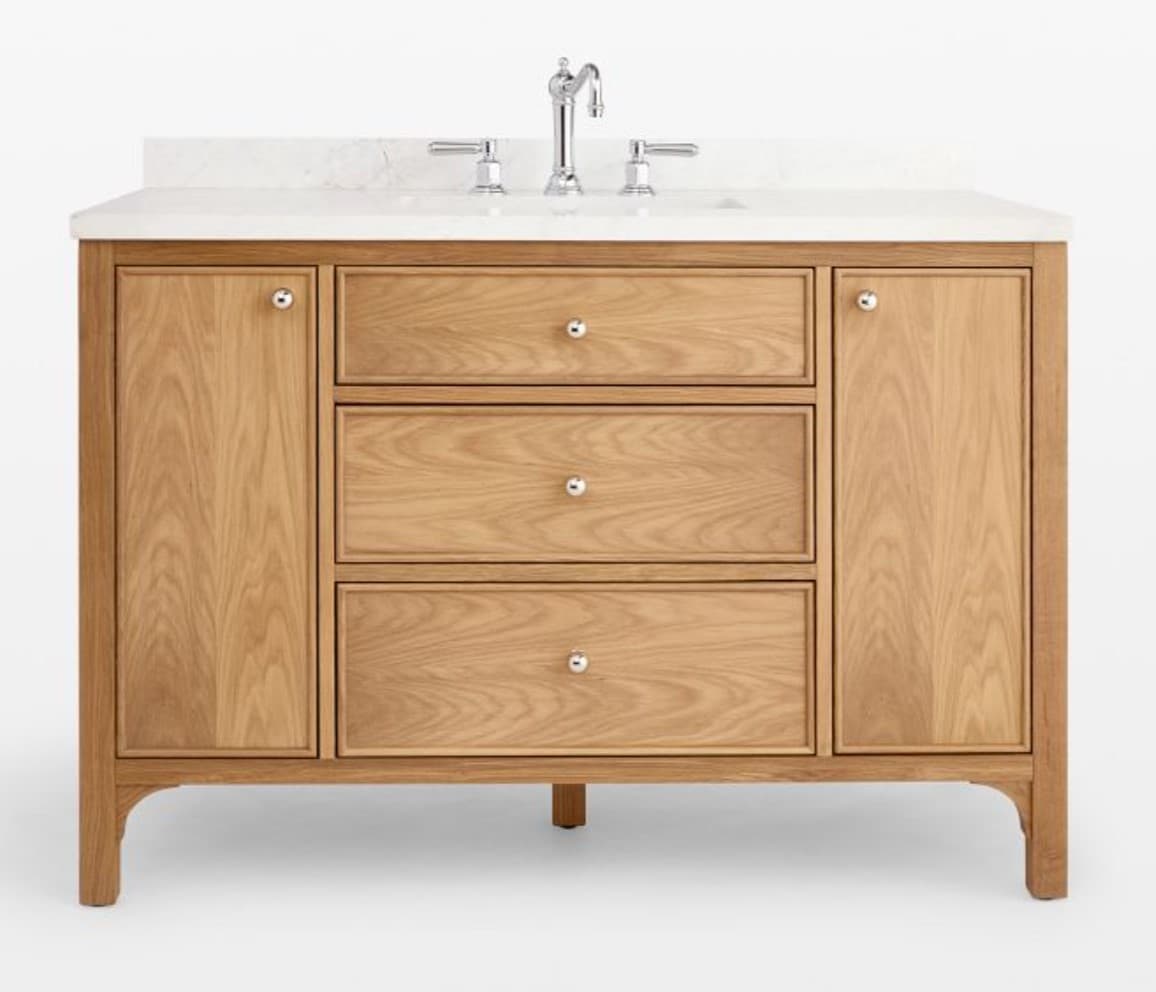 A wooden bathroom vanity with a white countertop and a sink faucet. The vanity features two cabinet doors on the sides and three drawers stacked in the center. It is supported by four legs, with the front two legs having a slightly curved, tapered design. — 3D model
