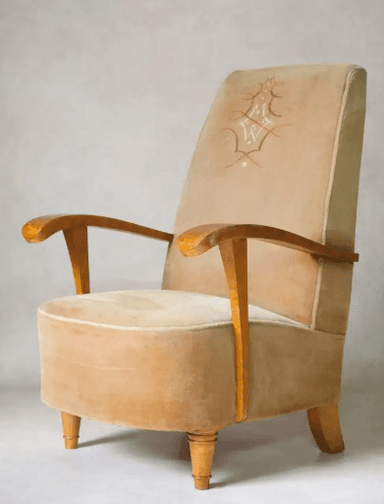 A vintage armchair with a high back and upholstered in a light brown, velvety fabric. The armrests are made of polished wood, featuring a curved design. The legs are also wooden, with decorative turned details on the front legs and a more modern, angled design on the back legs. — 3D model