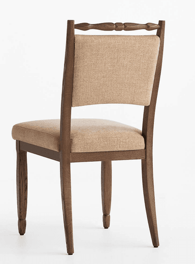 A traditional wooden dining chair featuring an upholstered seat and backrest, and a distinctive turned spindle top rail. The frame is made of dark brown wood, possibly oak, with visible grain. The seat and back are padded and covered in a light beige, textured fabric. The legs are tapered, with the back legs subtly splayed. — 3D model