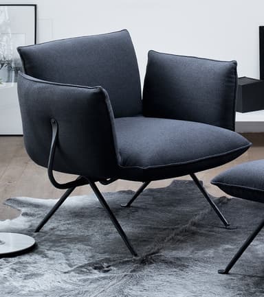 A modern dark gray upholstered lounge chair with a minimalist black metal frame. It features plush, separate cushions for the seat, back, and arms, along with an additional lumbar cushion. The frame consists of slender, angled legs. — 3D model