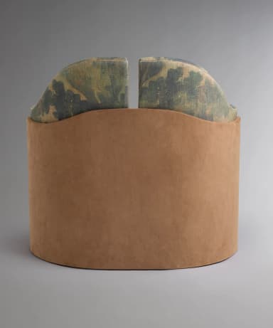 A single armchair with a rounded, upholstered body. The main upholstery features a large-scale floral or botanical pattern in muted greens, blues, and beige tones. The sides of the chair are covered in a contrasting smooth, tan material, possibly suede or a similar textile. The base is a dark wood, possibly walnut or mahogany, with a curved, pedestal-like design. The back of the chair has a subtle wingback element. — 3D model