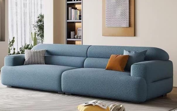 A modular sectional sofa with a light blue textured fabric upholstery. The sofa features rounded armrests and a deep seat. The backrest has horizontal segmented padding. Two decorative throw pillows are placed on the sofa: one with a black and white checkered pattern, and another in a burnt orange solid color. A third, smaller light blue pillow is also present. — 3D model